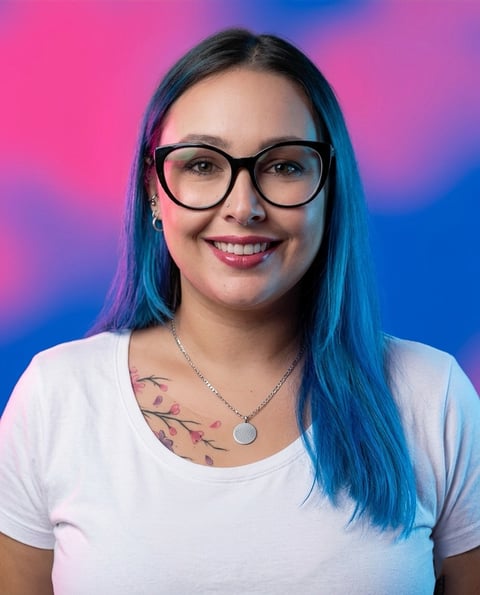 Woman with blue hair and glasses wearing a white t-shirt, smiling at camera against a pink and blue gradient background