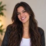 Smiling woman with long dark wavy hair wearing a black leather jacket and white top against a neutral background