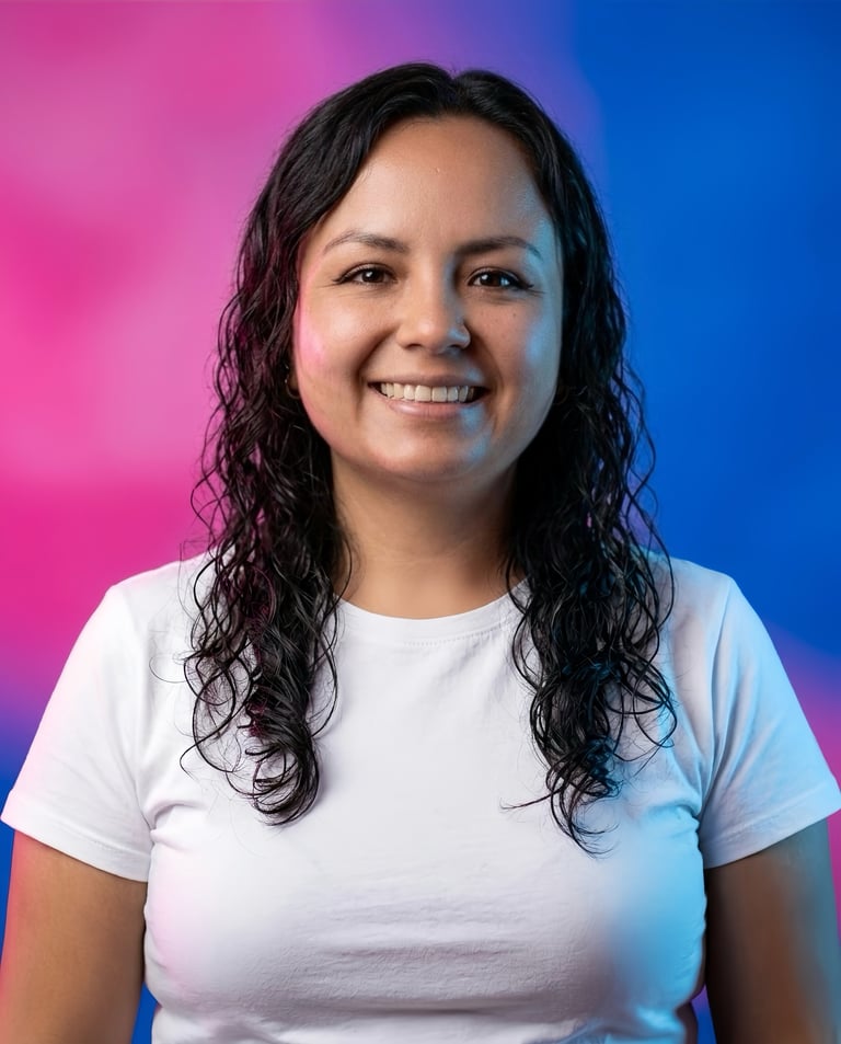 Smiling woman with long dark curly hair wearing a white t-shirt against a vibrant pink and blue gradient background